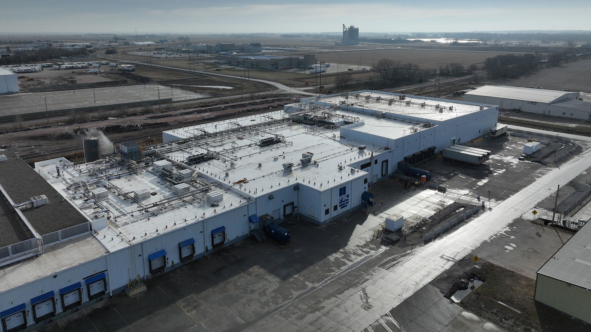 A large, white, rectangular meat packing facility seen from above among broader open fields.