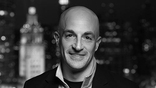A black-and-white headshot of a man with no hair