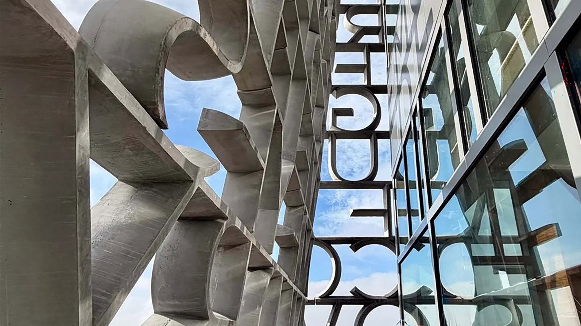 Close-up side view of the Obama Presidential Center exterior wall showing the custom concrete letters and glass window reflections.
