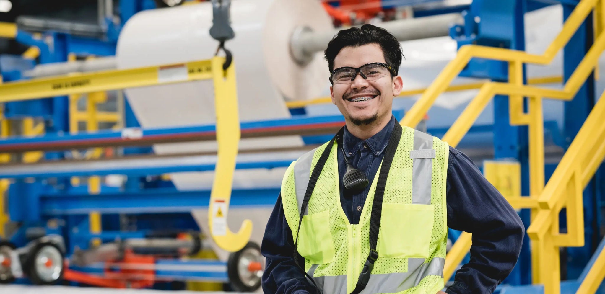 Un travailleur portant une veste de sécurité debout devant une grande machine industrielle