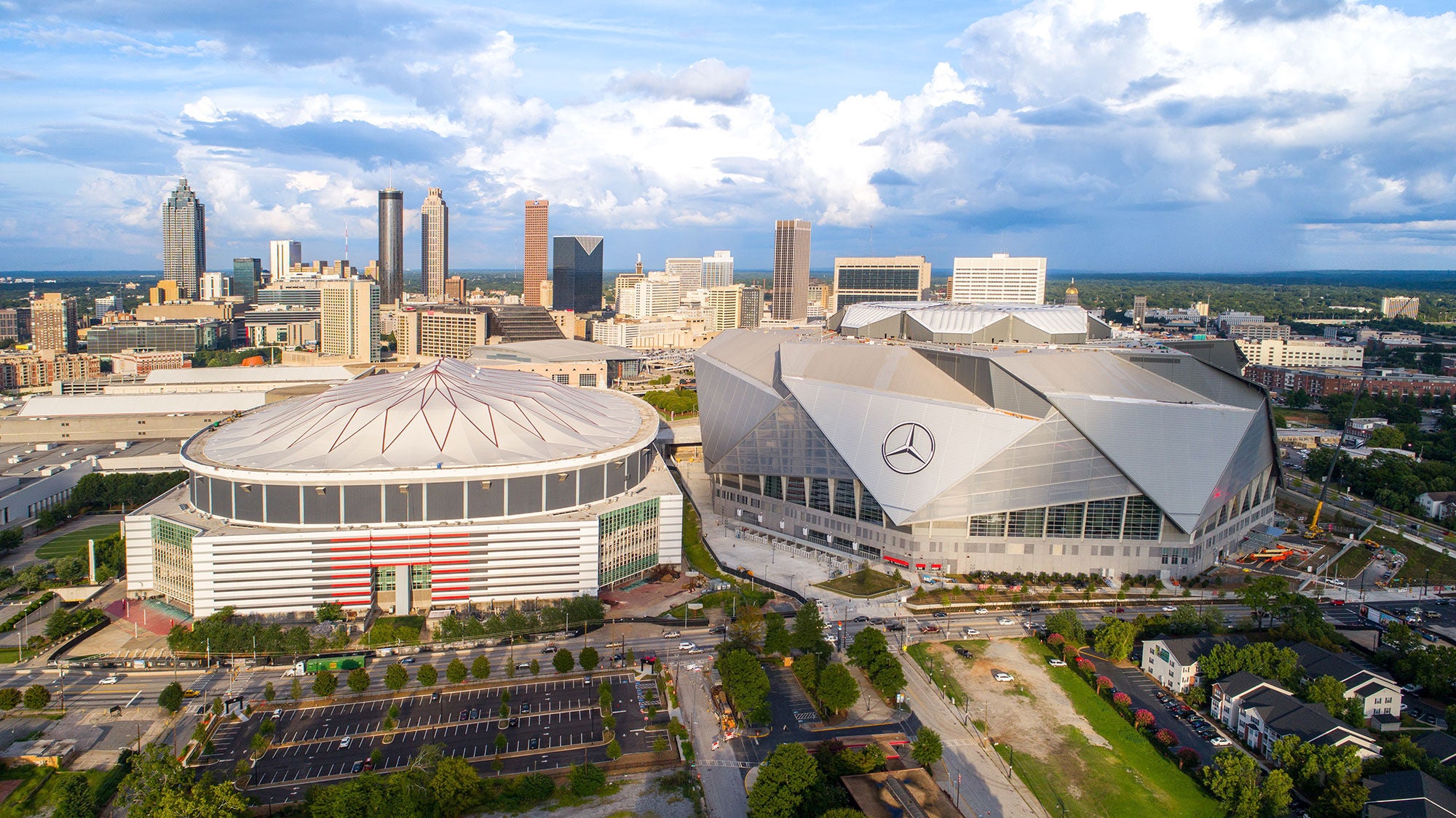Aerial view of Mercedes-Benz Stadium and the Georgia Dome next to the downtown Atlanta skyline under a cloudy sky.