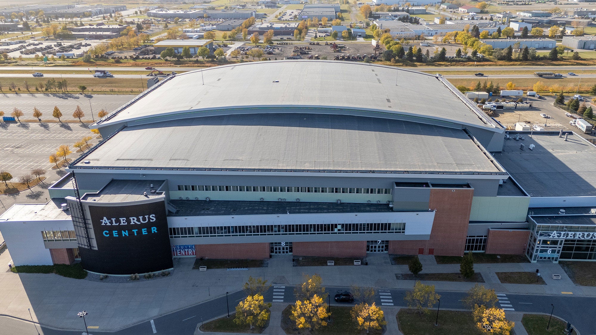 Aerial view of the Alerus Center multi-purpose stadium in Grand Forks, North Dakota, showing its large grey roof and surrounding parking lots.