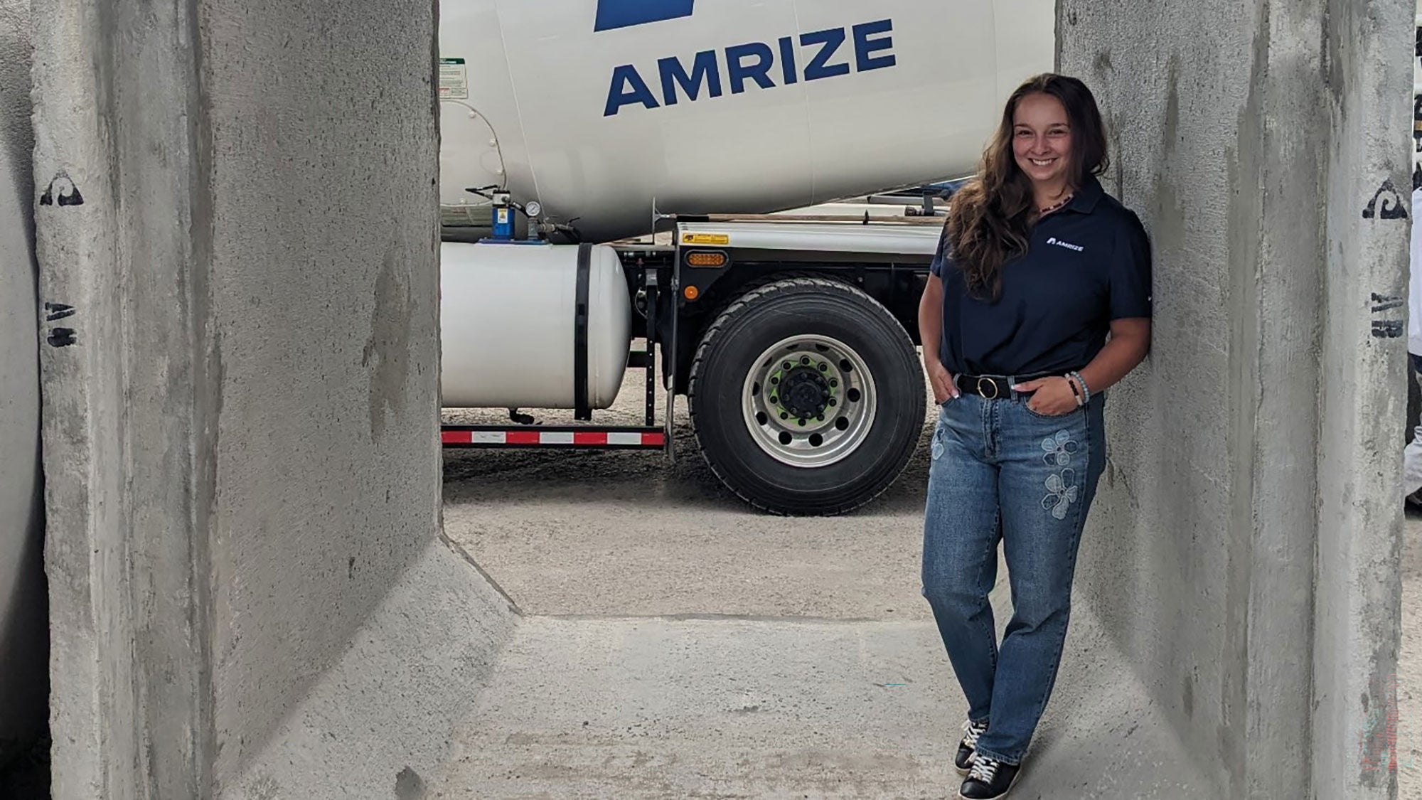 Amrize team member Skylar Yanke posing at the Amrize concrete pipe plant with industrial transport equipment in the background.