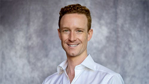 Headshot of Chris Bird wearing a white button-down shirt, smiling against a white background.