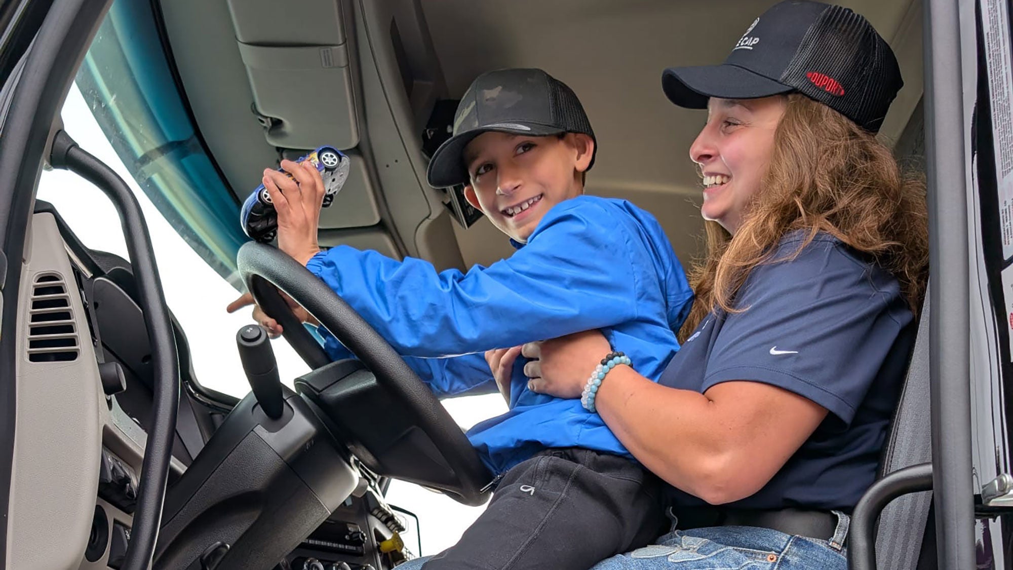 Mother and son smiling together inside the cab of a ready-mix truck.