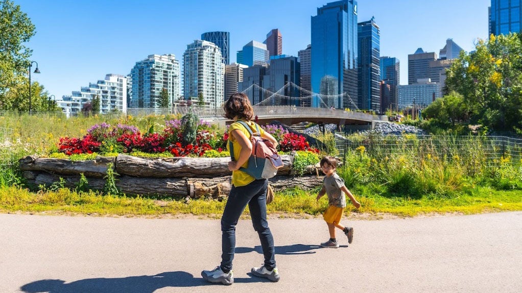 A woman and child walk through an urban park on a sunny day