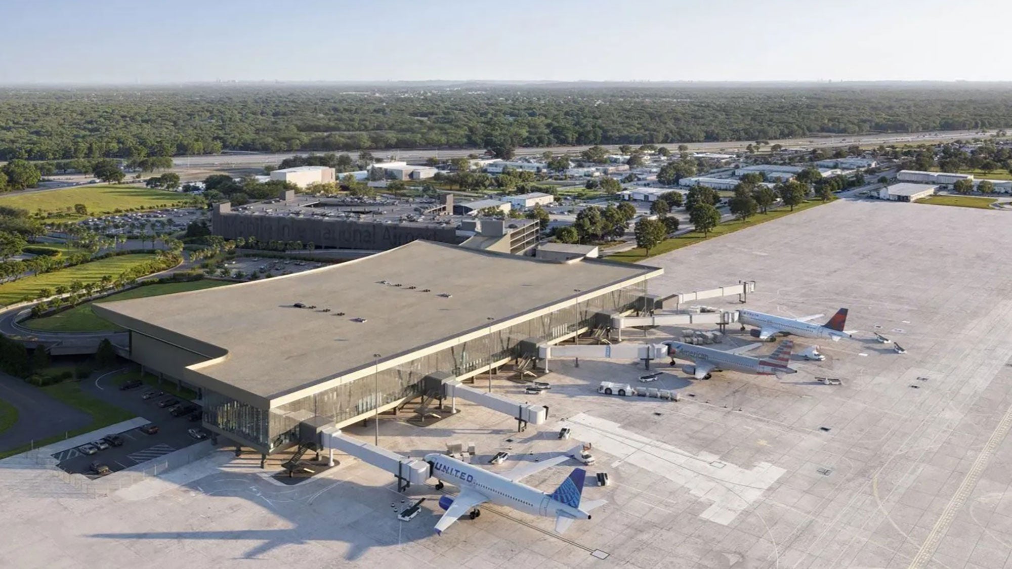Aerial view of Mobile International Airport's new terminal with several planes parked at gates. The terminal is surrounded by greenery, roads, and distant buildings.