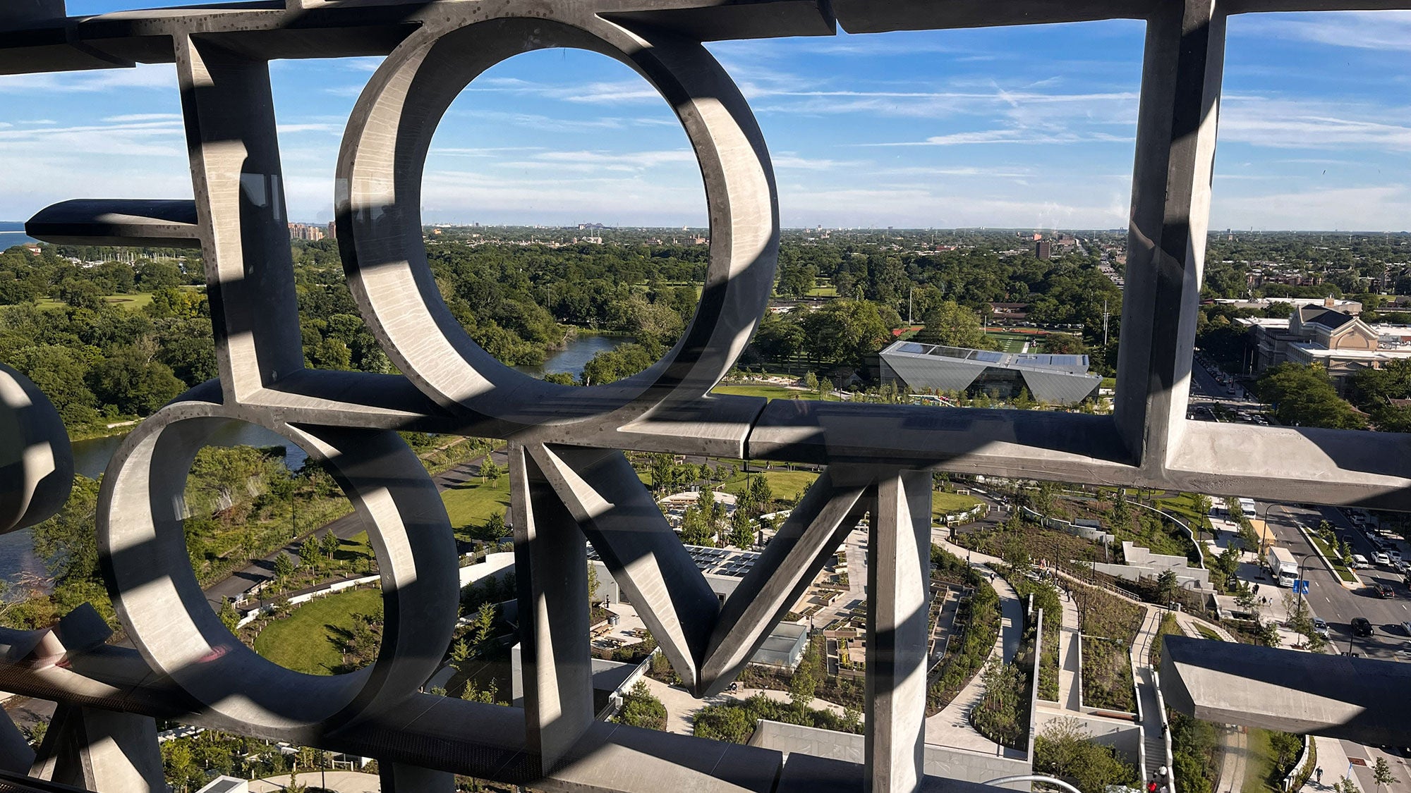 View of Jackson Park and surrounding campus grounds seen through the concrete lettered window screen at the Obama Presidential Center.