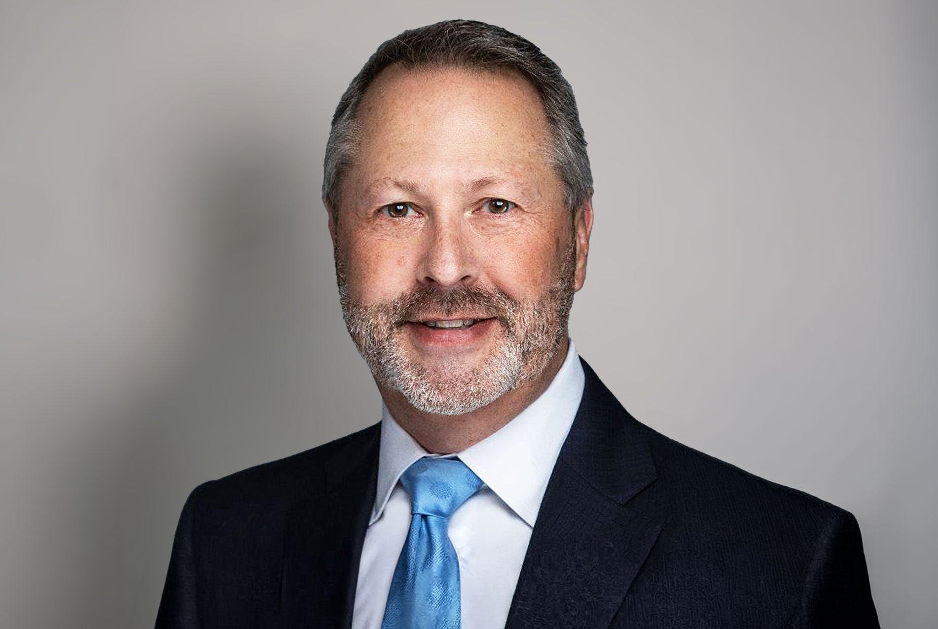 Headshot of Don P. Newman featuring a man in a black suit with a blue tie.