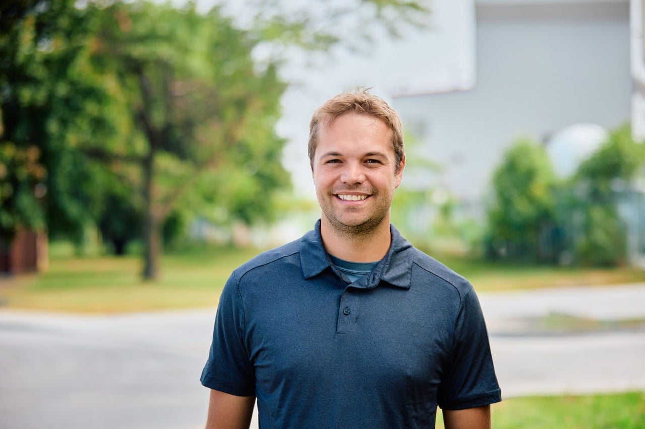 Man smiling at camera in front of blurred residential background