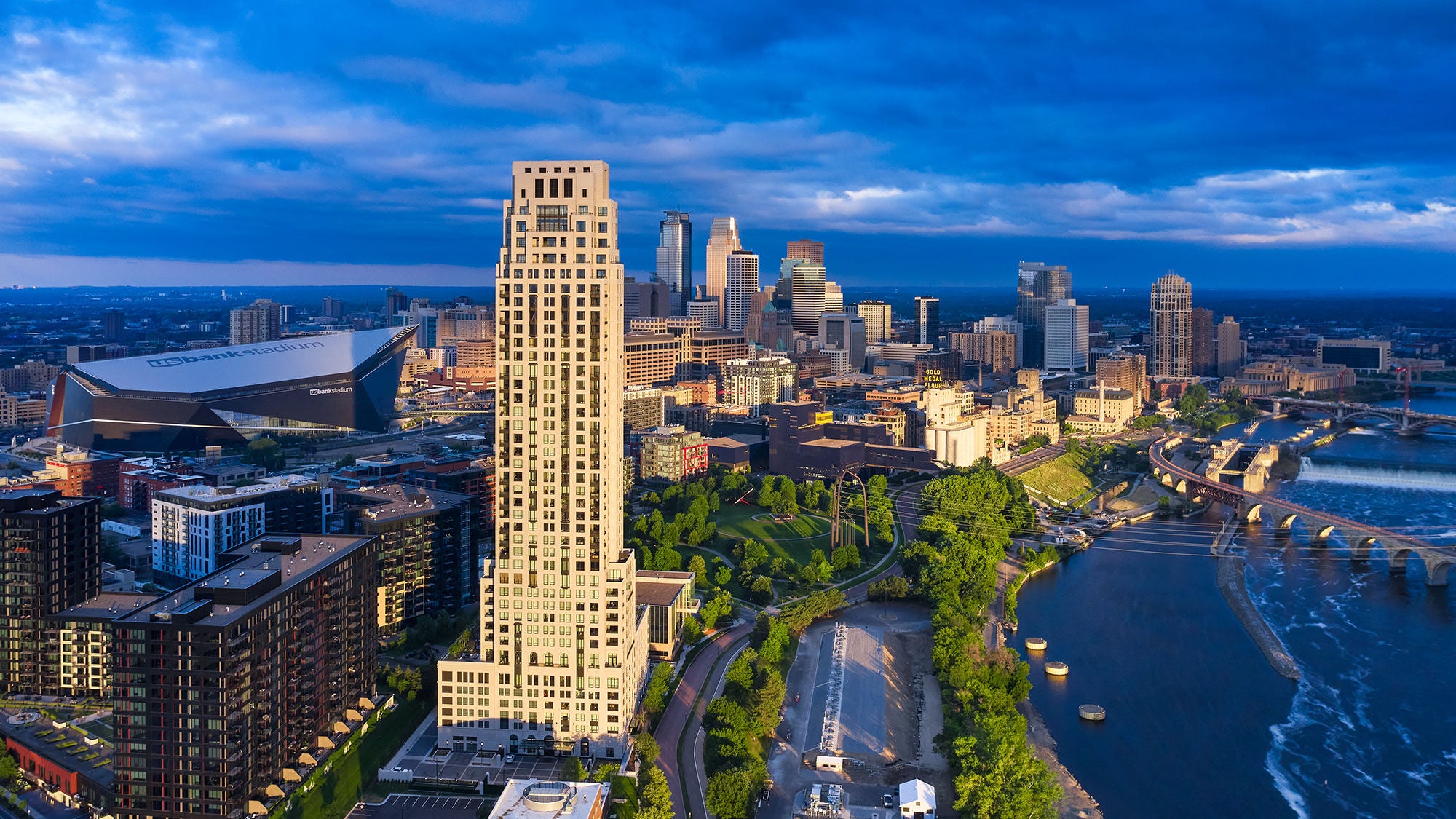 A tall concrete skyscraper next to a blue river as seen from a distance