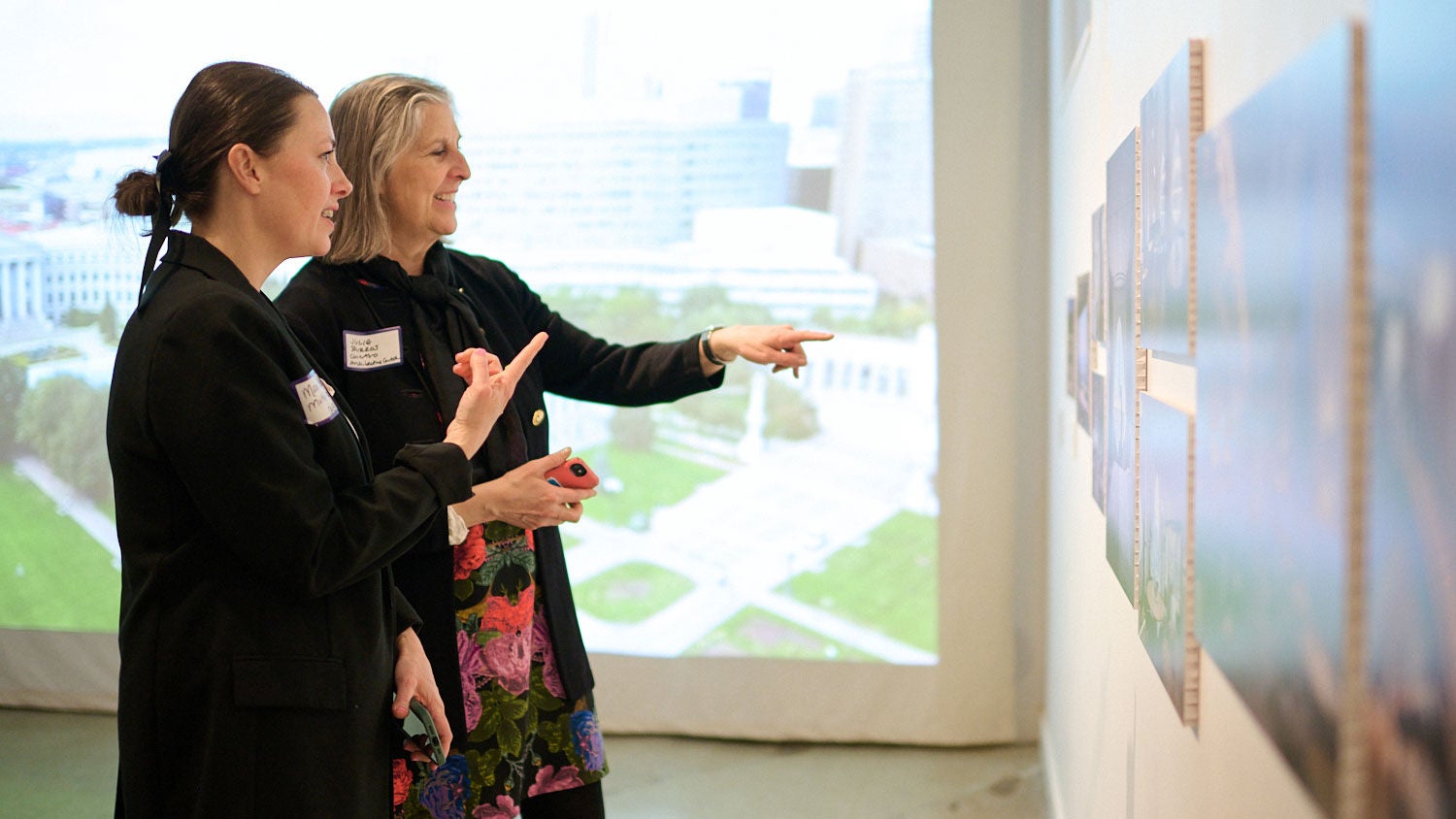 Two visitors at Studio Gang’s Biennial exhibit point to artwork on the wall.