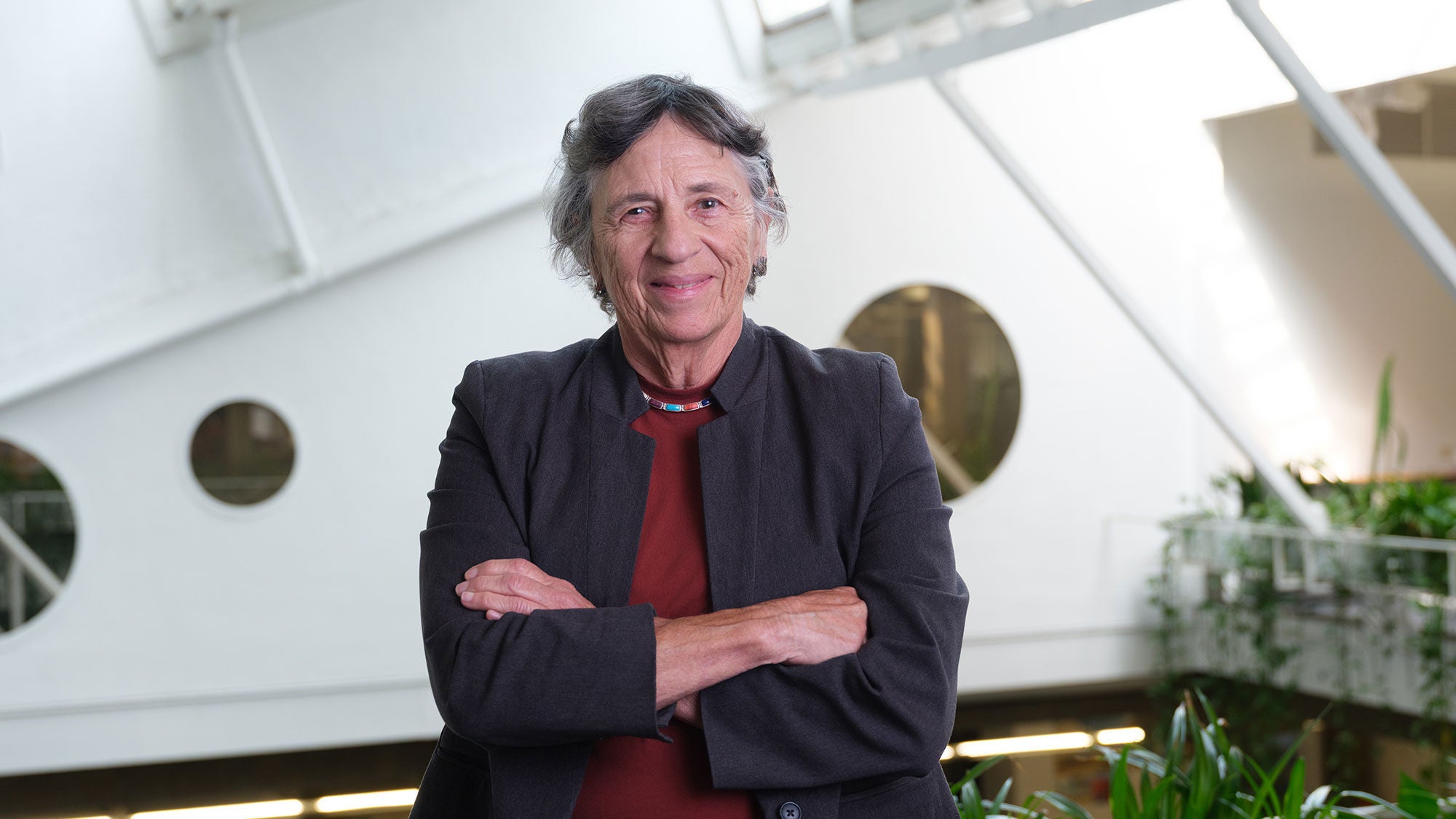 An architect in a dark overshirt and red undershirt with their arms folded.