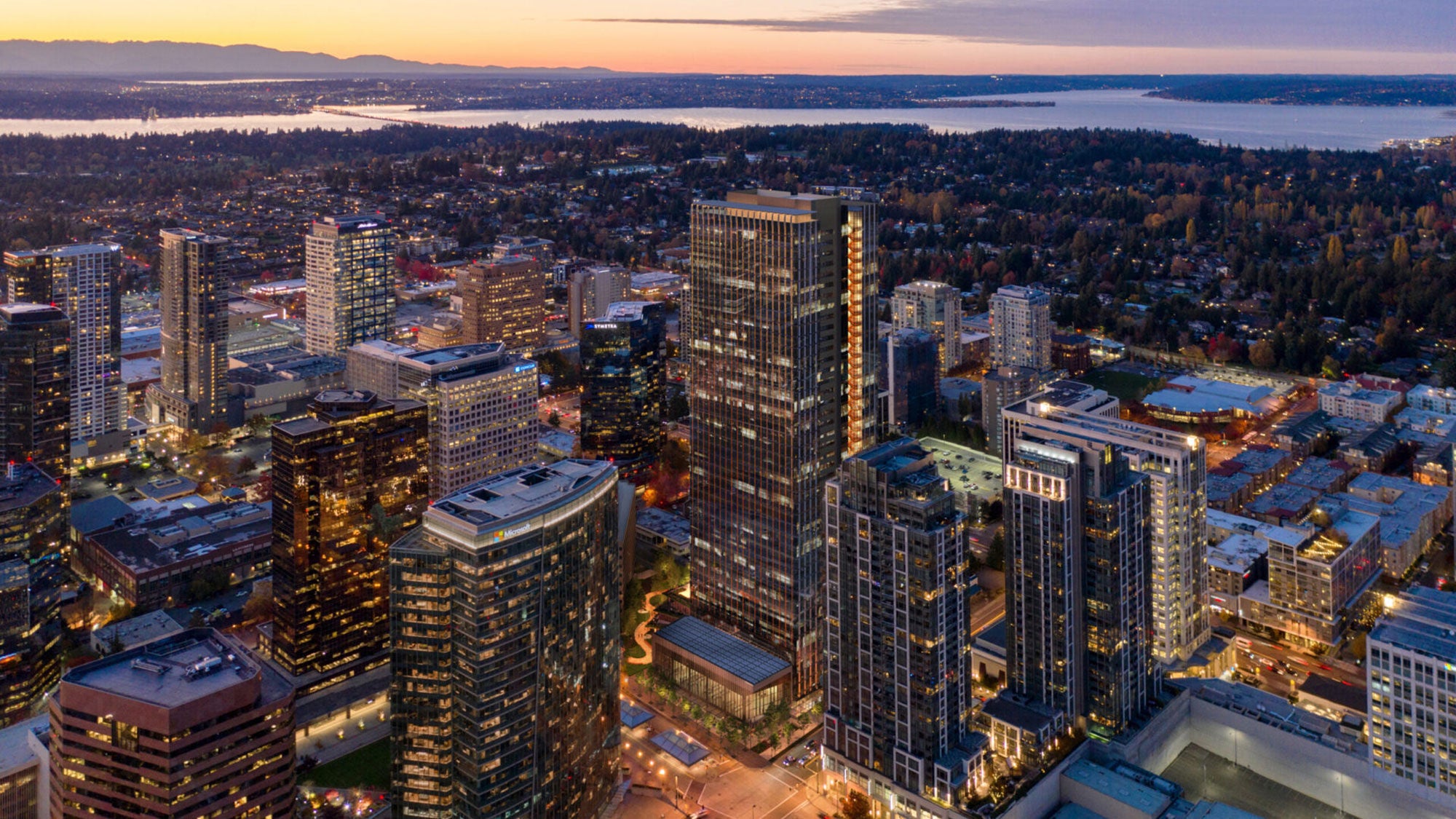 Tall modern skyscraper with a glass facade, standing among other high-rise buildings at sunset
