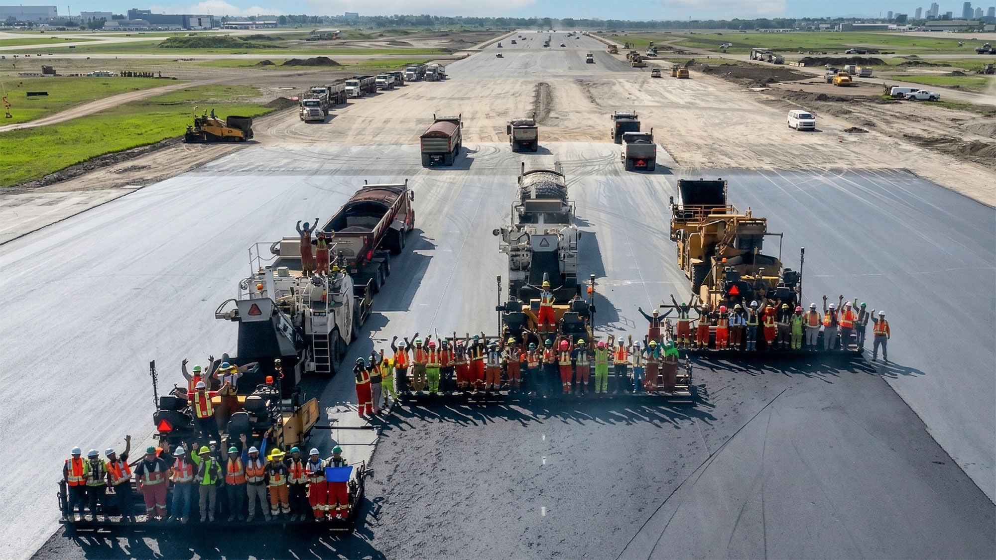 A collective of construction workers posing with asphalt pavers on a wide runway project at YYC Airport.