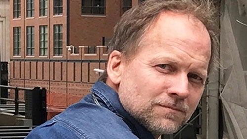 Alexander Kitchin wearing a blue denim shirt outside with a building behind him.