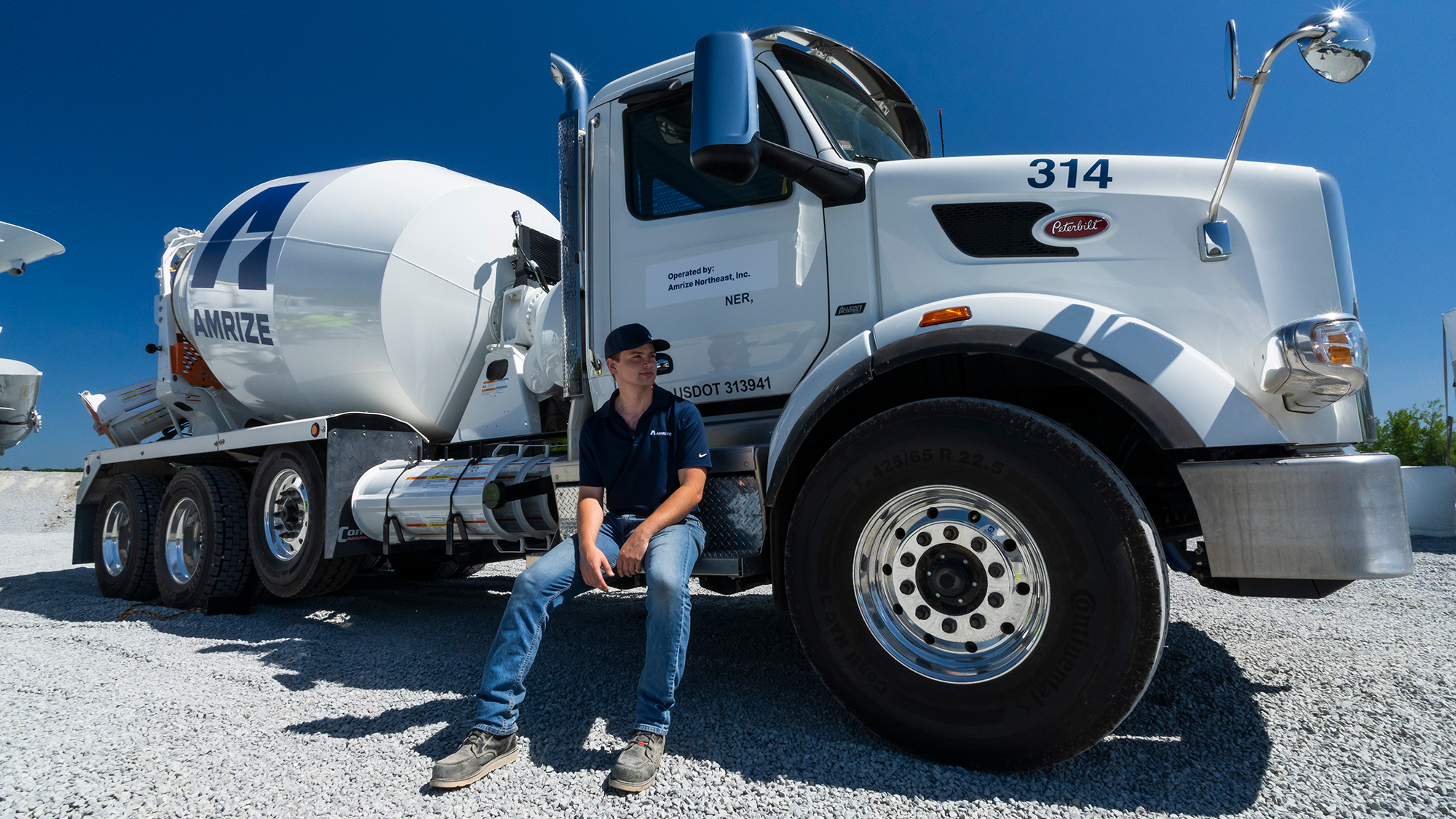 Event Photography Event PhotograpA man wearing an Amrize cap and shirt sitting on the foot step of a cement truckhy