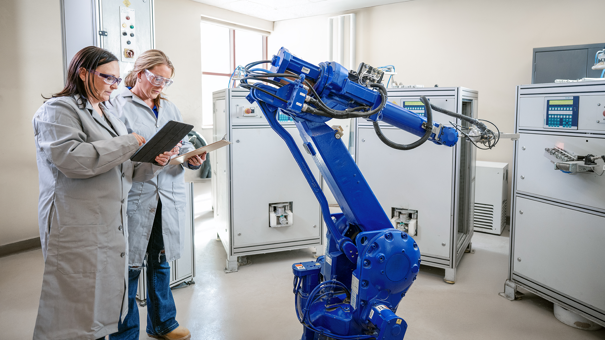 Two women in lab coats working with a large robotic arm