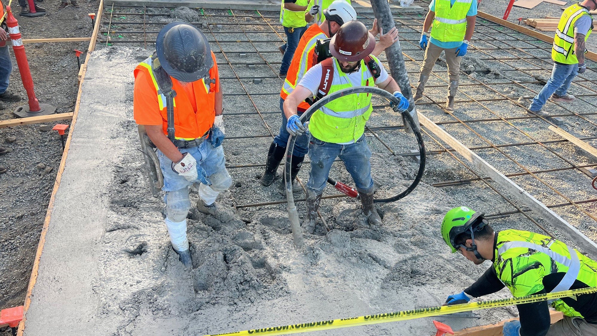 Several workers on a construction site test and place pumped concrete.