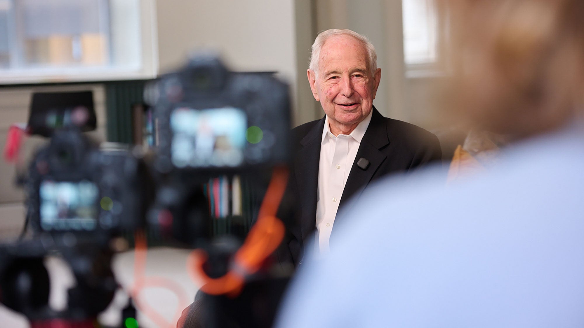 With two cameras and the interviewer in the foreground, a man sits being interviewed.